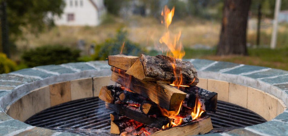Outdoor,fire,pit,with,burning,firewood,and,a,house,in